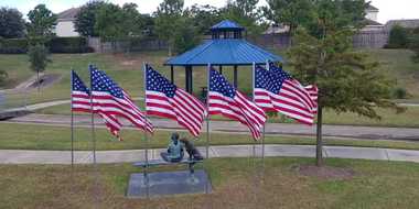 Statue of a young child sitting on a bench with two dogs surrounded by six american flags in front of a blue gazebo.