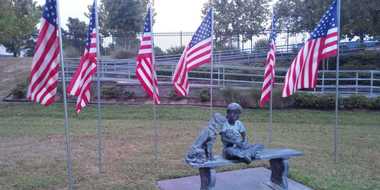 Statue of a young child sitting on a bench with two dogs surrounded by six american flags.